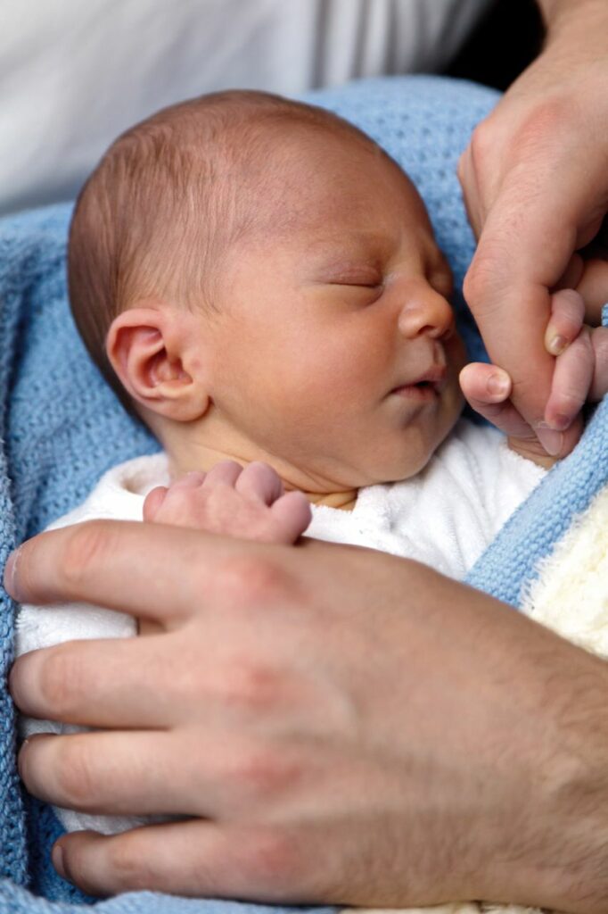 Un bébé endormi tient le doigt de sa maman.