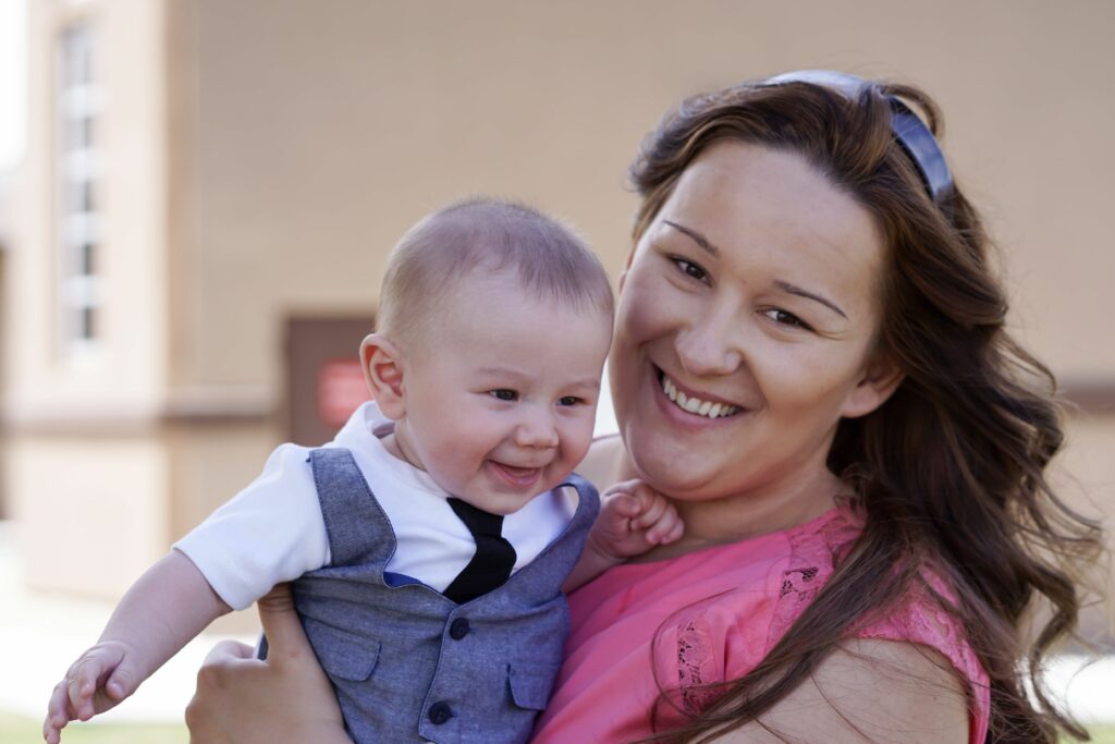 Une maman souriante tient son enfant de huit mois dans les bras